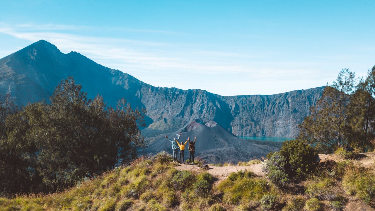 Three hikers raise their arms in joy at the crater rim of Mount Rinjani, Lombok, Indonesia.